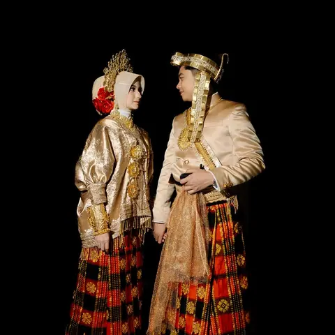 Cantika dan Deni berjas bersulam emas dan bersarung tenun merah-emas, saling berhadapan dengan latar hitam