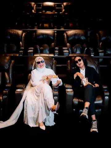 Pasangan prewedding berkacamata hitam dengan popcorn di kursi bioskop