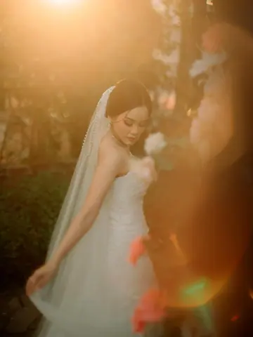 Pengantin wanita dengan veil panjang dan gaun strapless, disinari cahaya emas matahari sore